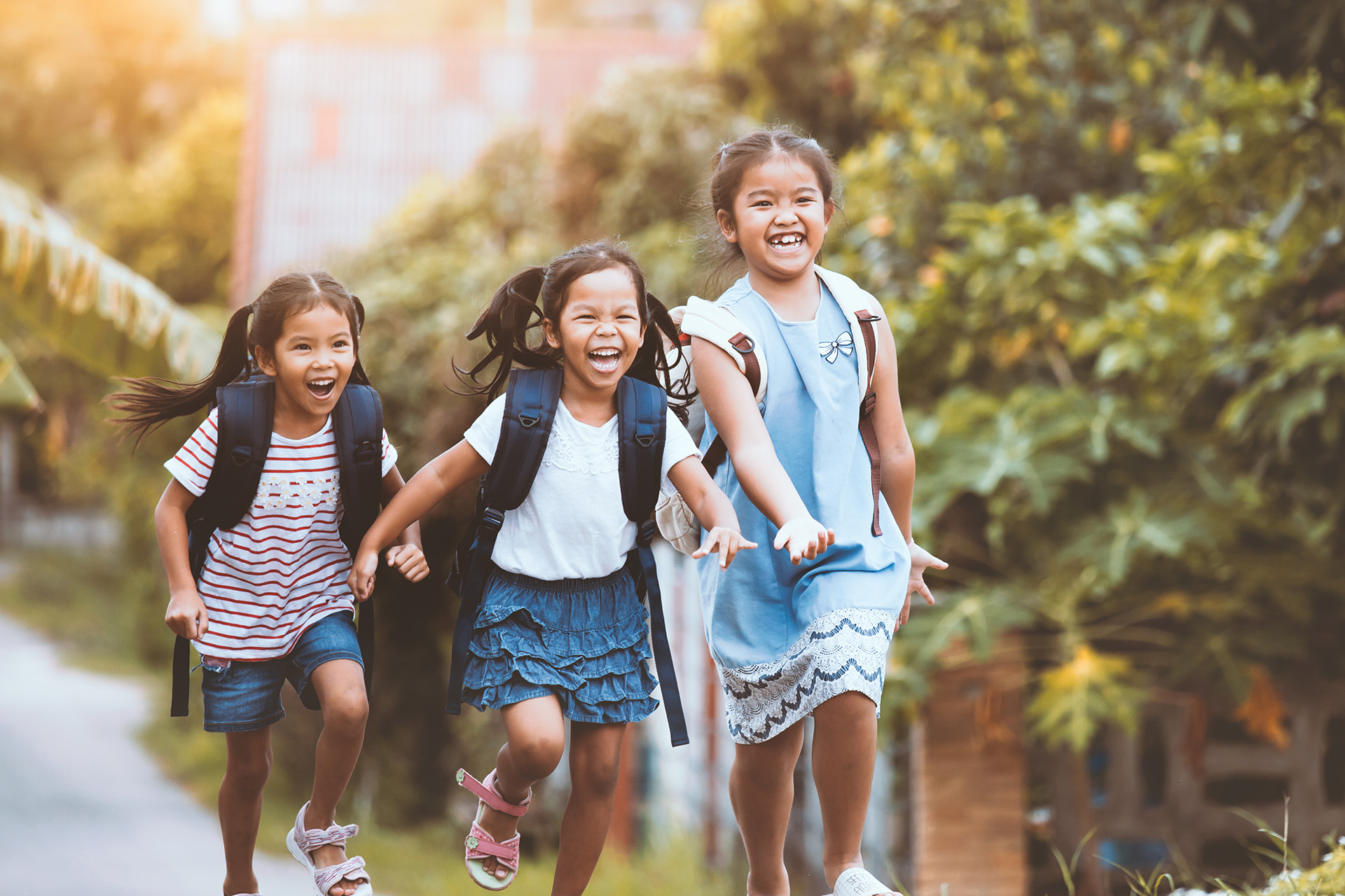 Three young girls with backpacks running on sidewalk
