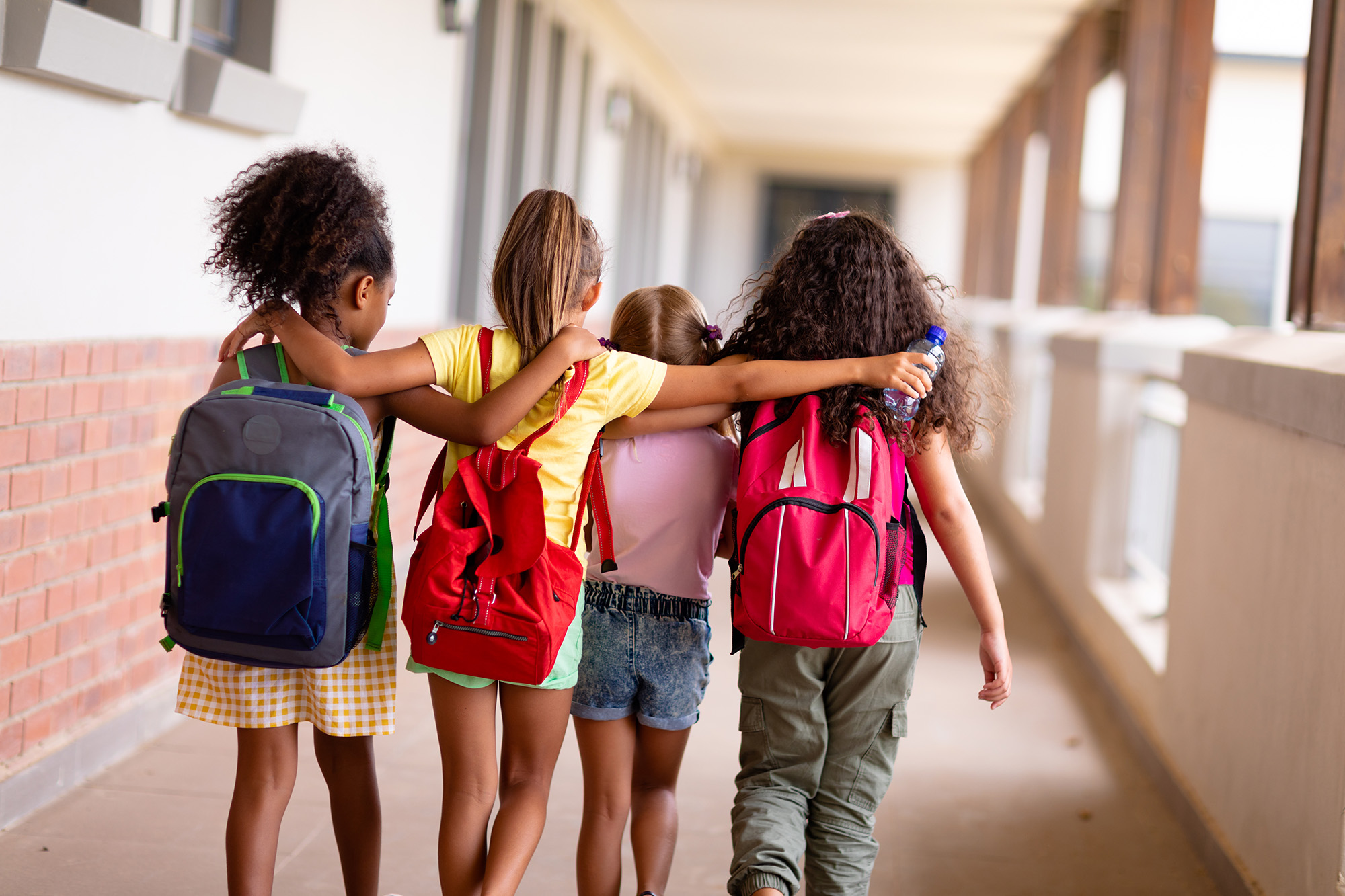 Rear view of multiracial elementary schoolgirls with backpacks a
